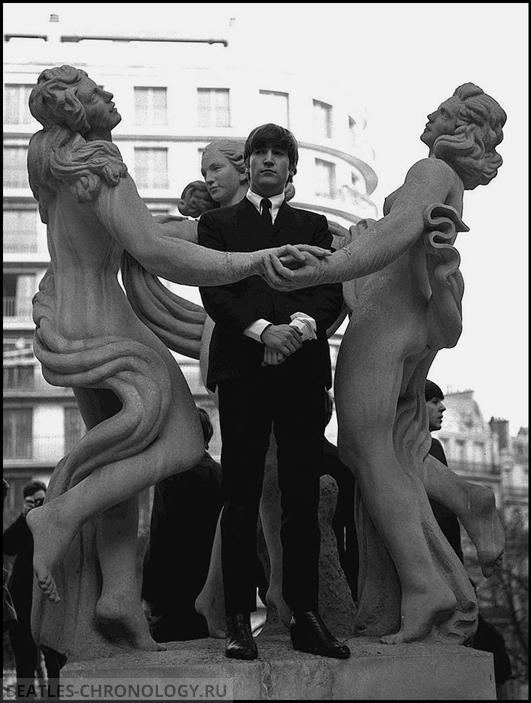 Paris, France, 1964. John Lennon poses between two statues during the visit to Paris of the British pop group The Beatles.